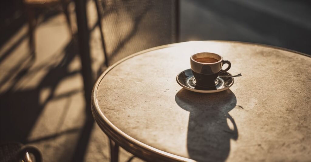 Tazzina di caffè del pomeriggio su un tavolino urbano elegante, con luce calda e ombre lunghe che evocano un momento di quiete e benessere. di dm plus studio