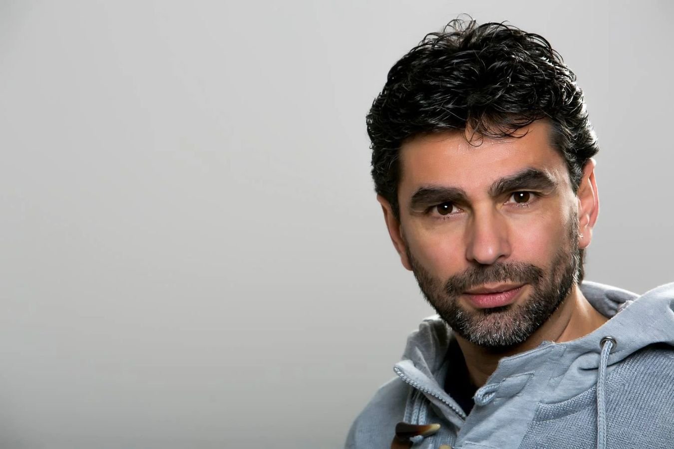 Ritratto di Damiano Macaluso, sviluppatore web e UX designer, in primo piano con felpa grigia e sguardo diretto verso l’obiettivo. Luce neutra e fondo sfumato. dmplus. dm+. Damiano Macaluso