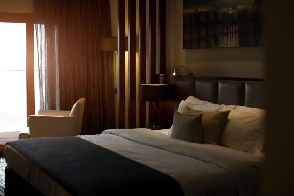 Interno di camera d’albergo elegante con letto matrimoniale, luce naturale e arredo moderno. dmplus. dm+. Damiano Macaluso